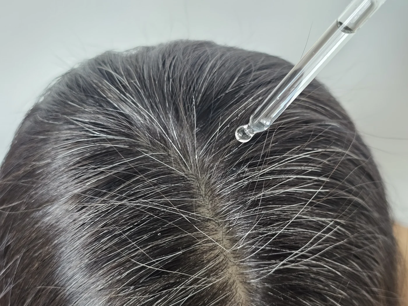 A dropper applying Crowned serum directly along the part line A dropper applying Crowned serum directly along the part line